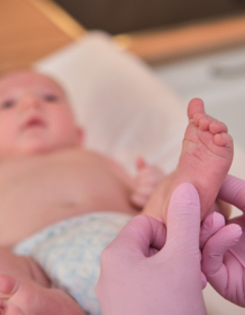 The doctor does gymnastics and massage to a newborn baby. Nurse in uniform doing warm-up exercises to the child